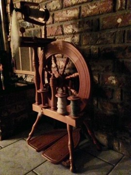 A spinning wheel, standing on tiles, with a brick wall backdrop