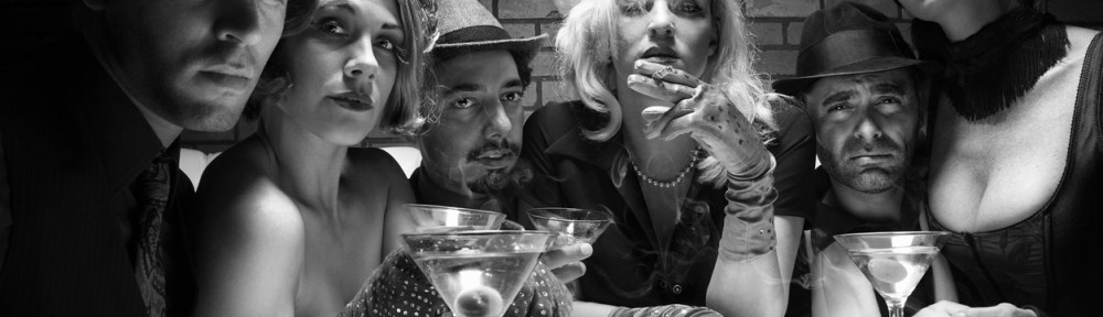 Group of Caucasian adult retro males and females sitting at table in lounge looking at viewer.
